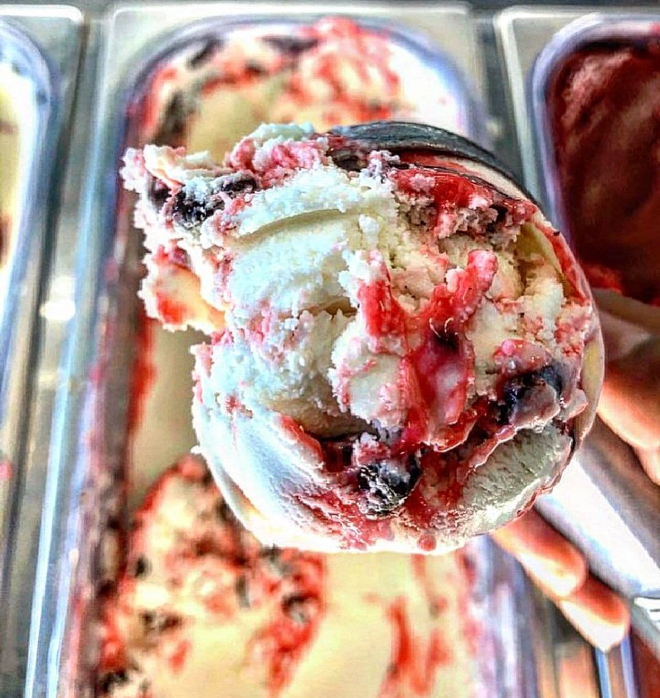 A scoop of berry-swirled gelato lifted from the case at Battr, with more flavors in trays behind it.